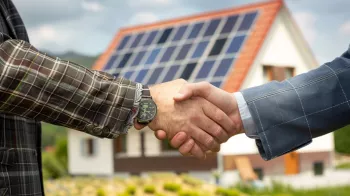 Zwei Personen geben sich die Hand vor einem Haus mit Solarpanelen auf dem Dach, symbolisiert eine Vereinbarung oder den Abschluss eines Geschäfts im Bereich der Solarenergie.